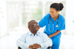 a black nurse standing next to a black patient sitting in a wheel chair