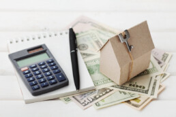 miniature home and calculator on top of pile of money